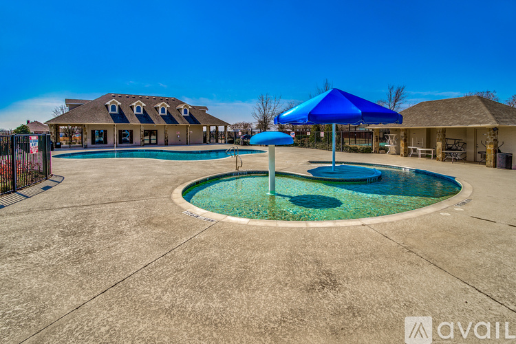 A large outdoor pool area with a blue umbrella and a fence.