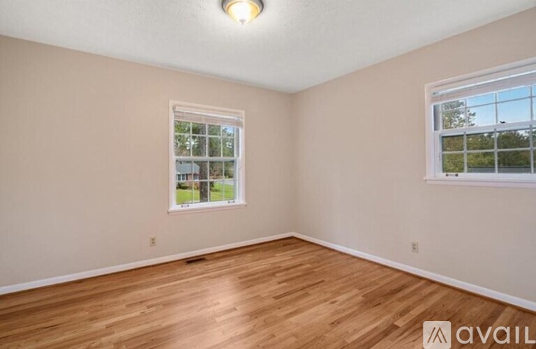 A room with wooden flooring and a window showing a view of trees and a house.