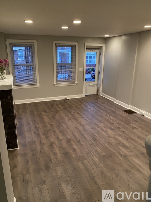 A room with wooden flooring and a fireplace with a vase of flowers on top.