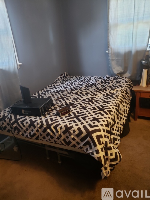 A bed with a black and white patterned comforter and a black box on the bed.