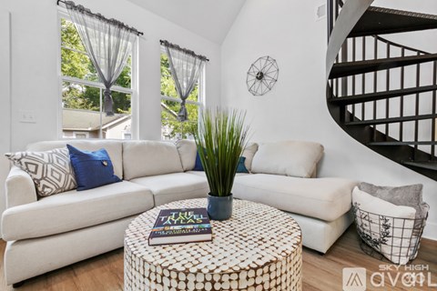 A living room with a white couch, a round table with a book on it, and a black spiral staircase.