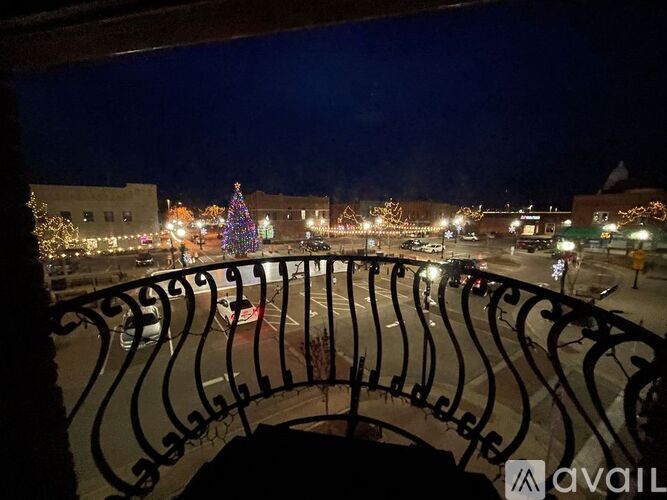 A balcony railing overlooks a street with Christmas lights and a lit-up tree.