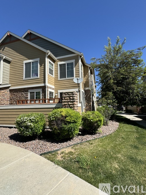 A house with a brown and beige exterior has a small front yard with bushes and a sidewalk.