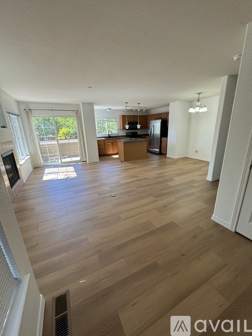 A spacious living room with wooden flooring and a kitchen area in the background.