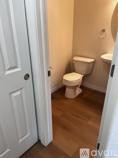 A white toilet in a small bathroom with wooden floors and a white door.