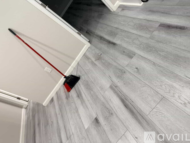 A broom is leaning against a wall on a wooden floor.