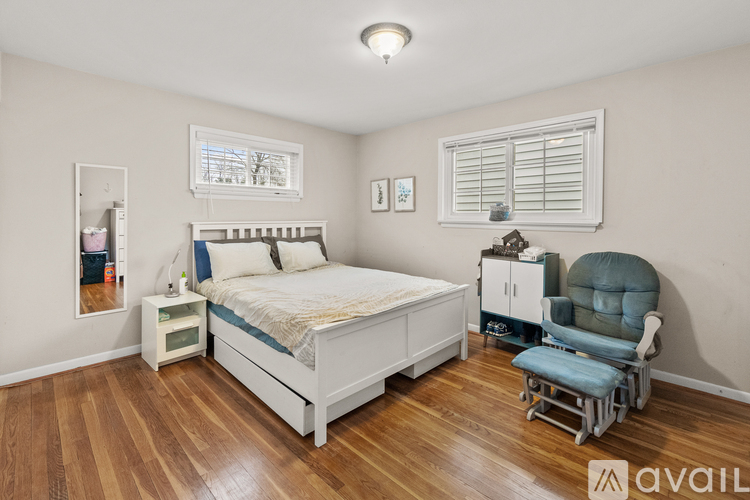 A bedroom with a bed, chair, and wooden floors.