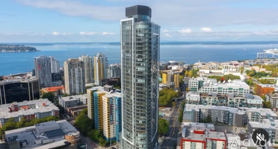 A cityscape with a tall building in the center and a body of water in the background.