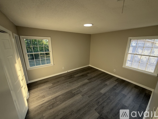 A room with wooden flooring and two windows.