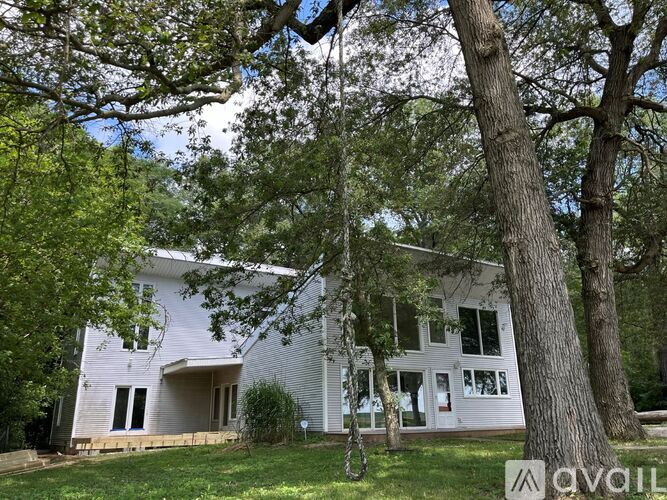 A white house with a porch and a tree in front.
