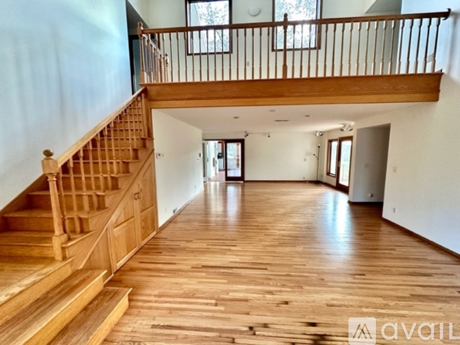A spacious room with wooden floors and a staircase leading to the upper level.