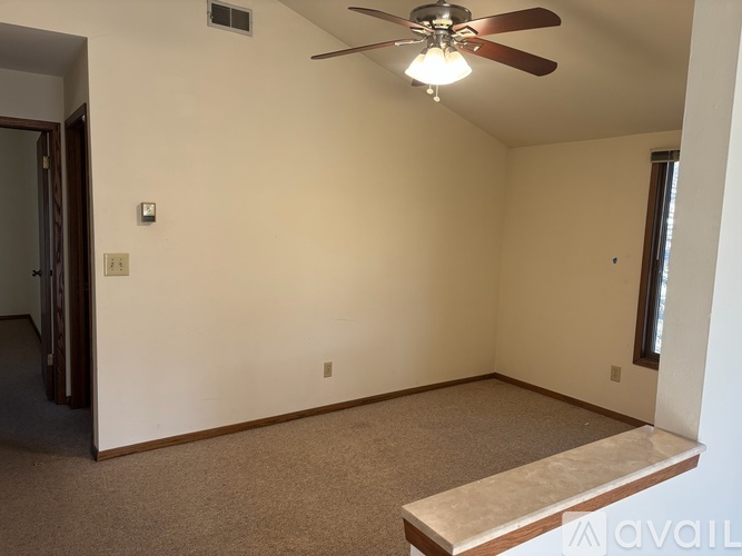 A room with a ceiling fan and a window with a view of a darker room.