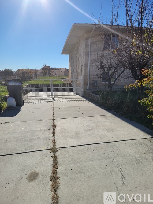 A concrete driveway leads to a house with a fence and trees in the background.