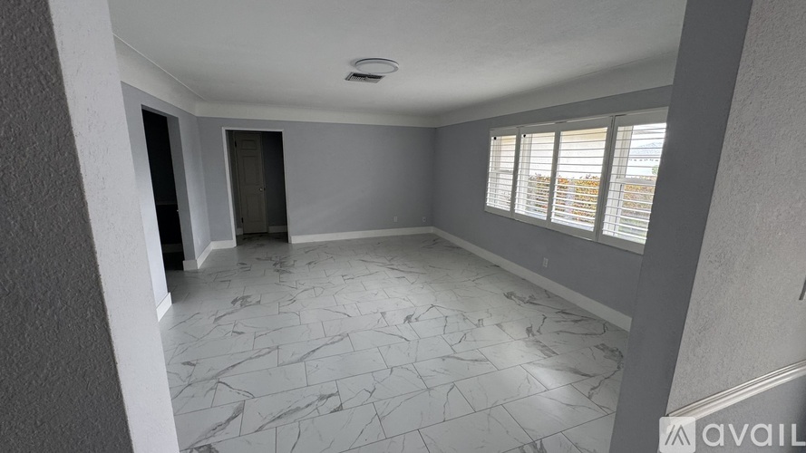 A spacious room with marble flooring and a window with blinds.