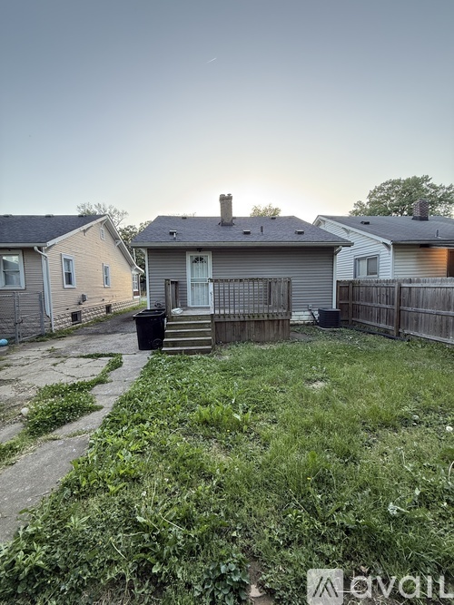 A backyard with a house, a fence, and a trash can.