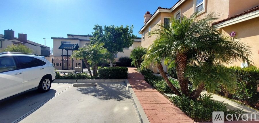 A white car is parked on the left side of a street with a building and trees in the background.