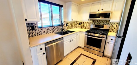 A kitchen with white cabinets and a black and white tiled backsplash.