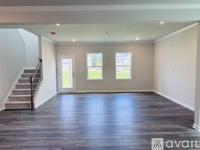 A spacious room with wooden floors and a staircase leading to the upper level.