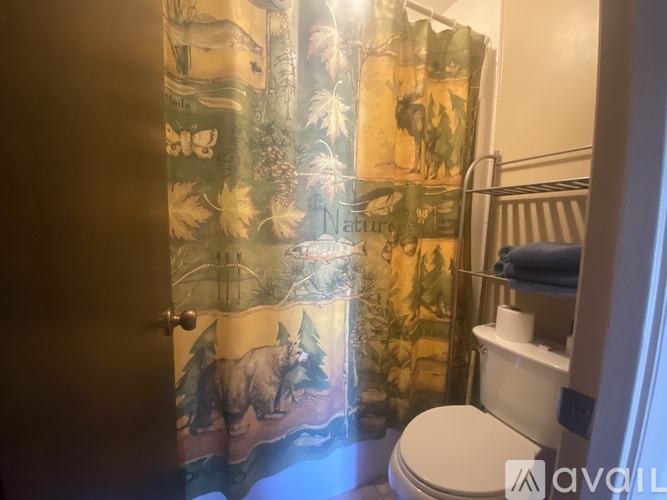 A bathroom with a toilet, a shower curtain with a bear and trees on it, and a towel rack with towels.