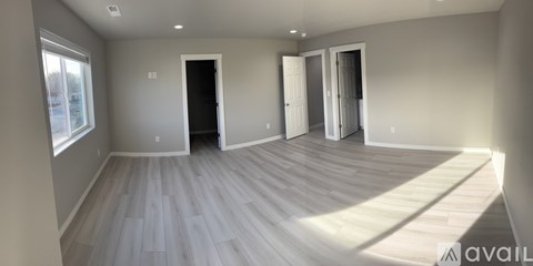 A spacious room with light wood flooring and white walls.