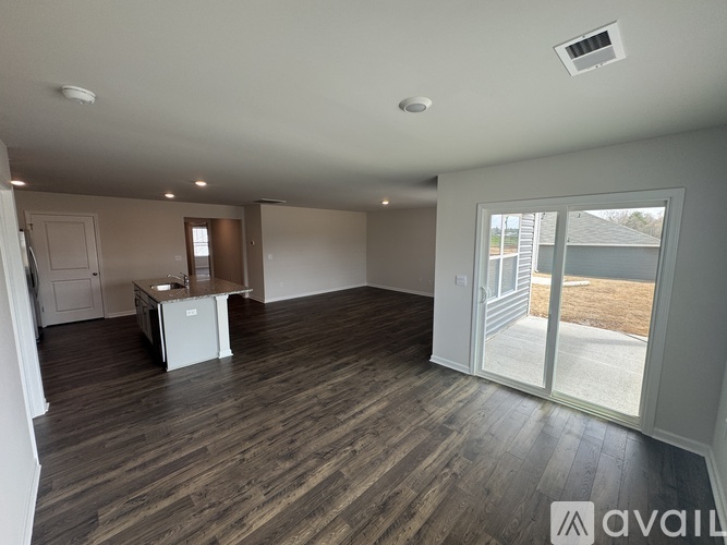 A spacious room with wooden flooring and a sliding glass door leading to a backyard.