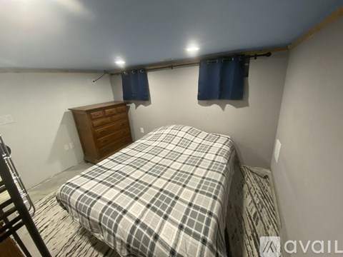 A bedroom with a bed, a dresser, and a window with blue curtains.