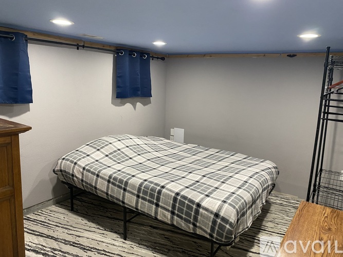 A bed with a plaid comforter is in a room with a wooden floor and a white wall.
