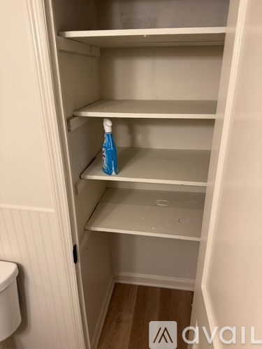 Empty white shelves in a pantry with a bottle of water on the bottom shelf.