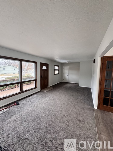 A room with a carpeted floor and a window overlooking a backyard.