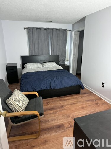 A bedroom with a bed, chair, and nightstand.