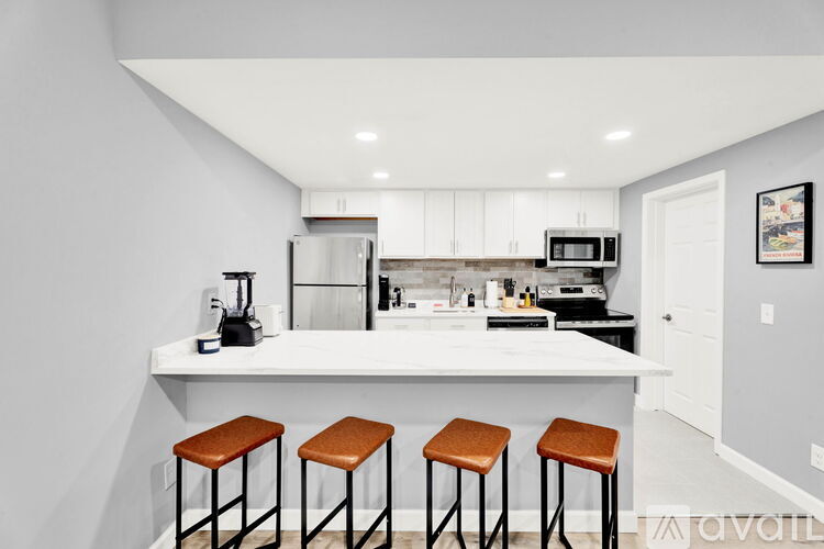 A kitchen with white cabinets and a white island with brown stools.