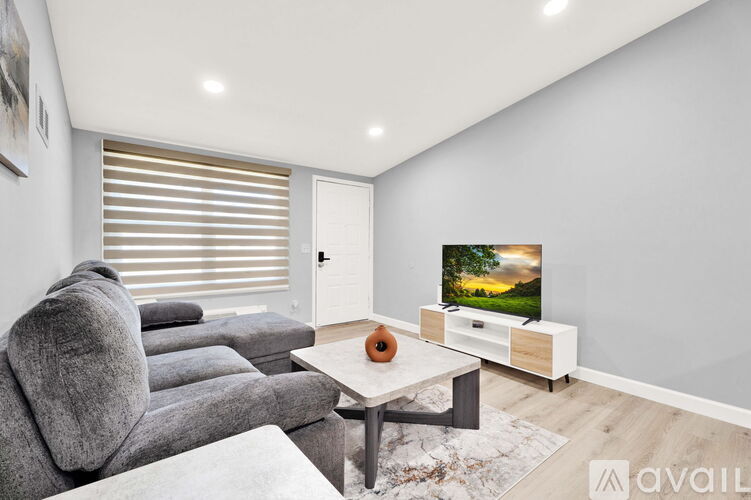 A modern living room with a grey sofa, a white coffee table, and a flat-screen TV on a wooden stand.