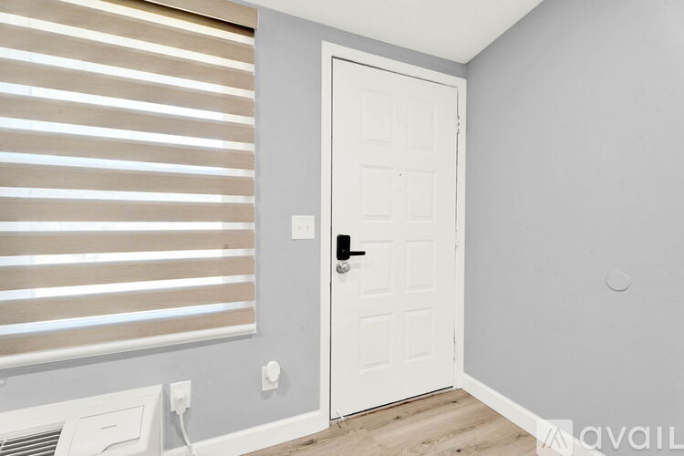 A white door with a black handle is in a room with a window covered by horizontal blinds.