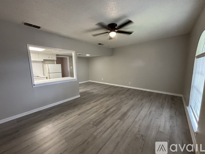 A spacious room with a ceiling fan and a window overlooking a kitchen.