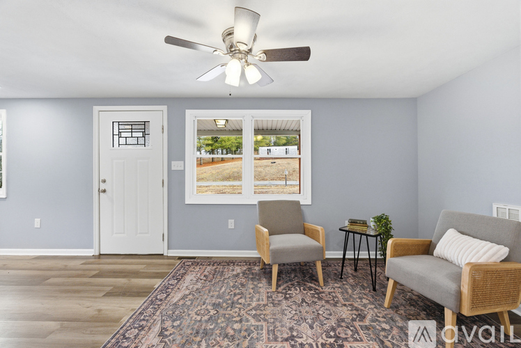 A living room with a rug, two chairs, and a ceiling fan.