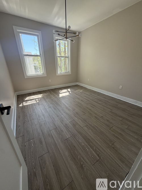 A room with wooden flooring and two windows.