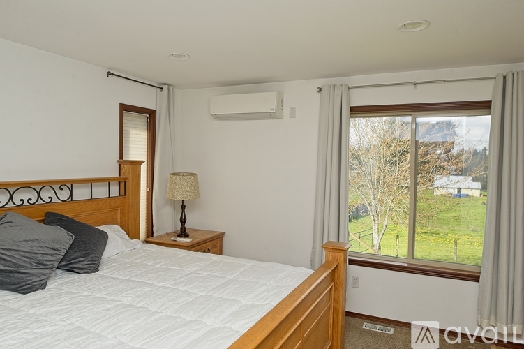 A bedroom with a large bed and a window overlooking a green landscape.