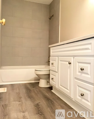 A white toilet sits in a bathroom with wooden floors and white cabinets.