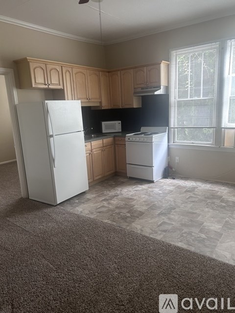 A kitchen with a white refrigerator, black microwave, white stove, and wooden cabinets.