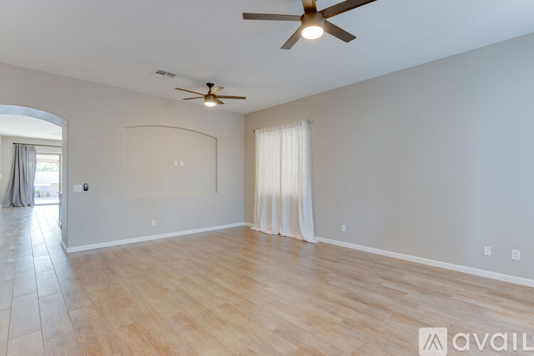 A spacious room with a ceiling fan and light, hardwood floors, and a window with curtains.