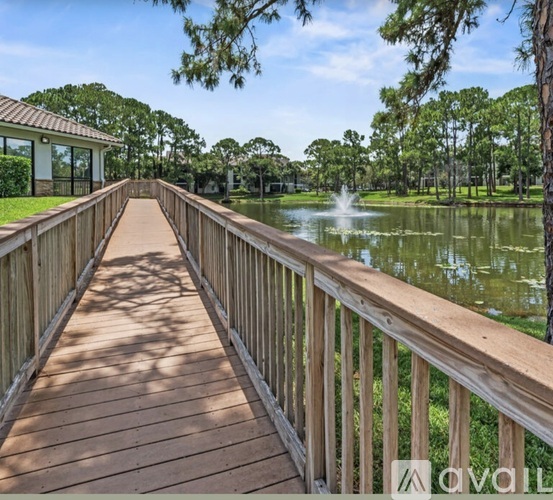A wooden bridge leads to a building with a fountain in the background.