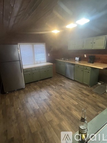 A bottle of alcohol is on a table in a kitchen with wooden floors and green cabinets.