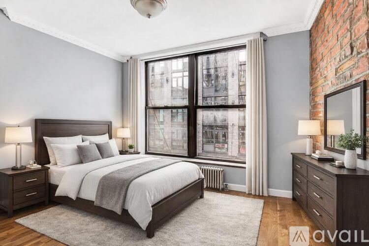 A bedroom with a large bed, two nightstands, and a window with a view of a cityscape.