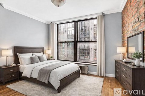A bedroom with a large bed, two nightstands, and a window with a view of a cityscape.