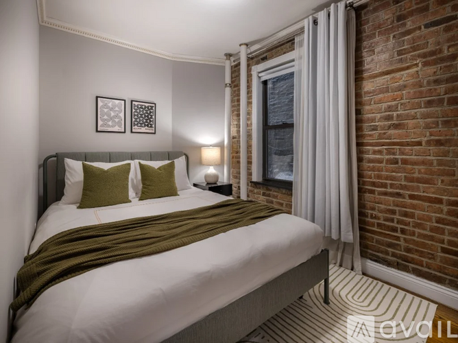 A bedroom with a bed, two pillows, a nightstand, and a window with a curtain.