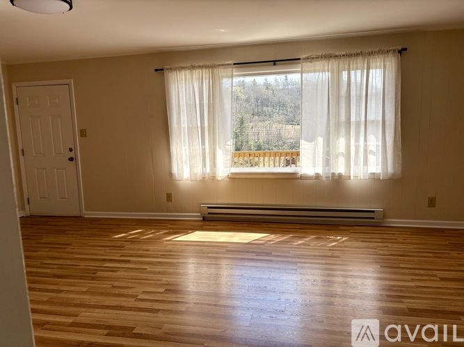 A room with wooden floors and a window with white curtains.