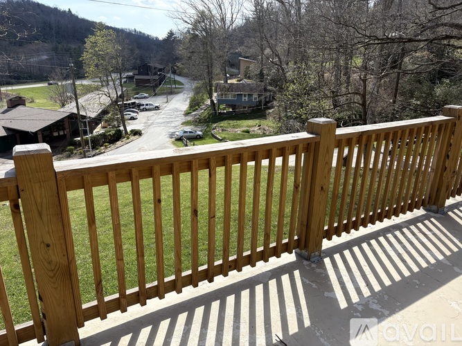 A wooden fence in front of a green lawn with a house and trees in the background.