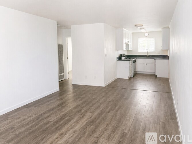 A spacious, empty room with wooden flooring and white walls.