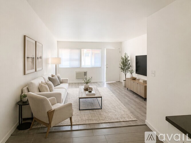 A living room with a white couch, a wooden chair, a coffee table, and a flat-screen TV.