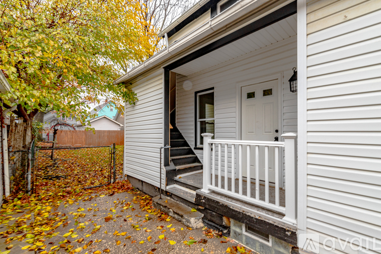 A white house with a porch and a tree with yellow leaves.